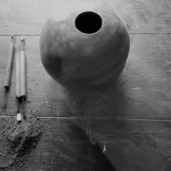 the image includes two hands on a rolling pin which is moving across a slab of clay