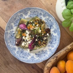 A table showing a plate of grilled vegetables, a basil plant and a bowl of nectarines