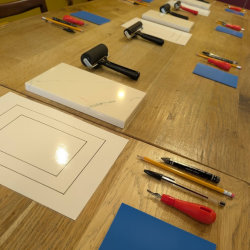 Table set up for a lino printing workshop, with rollers, lino and carving tools