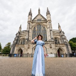 Miss Deane smiling in front of the grand west entrance of Winchester Cathedral.