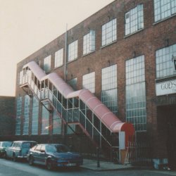 an image of the front facade of Chisenhale Dance Space in 1980, a brick warehouse with square glass windows and a red fire escape.
