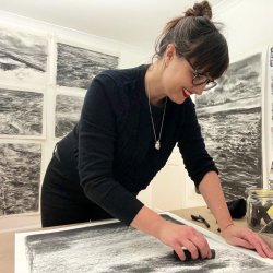 Liz Atkin drawing with charcoal in her studio with large charcoal drawings behind her