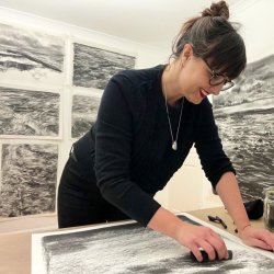 Liz Atkin drawing with charcoal in her studio with large charcoal drawings behind her