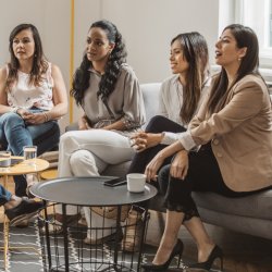 4 women in professional clothes sitting together on couches.