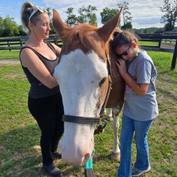 Horse with two people petting and resting on his shoulder.
