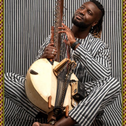 The image features Santou Susso sitting on the floor cross legged wearing black and white stripes holkding a kora, in front of a back a white striped background