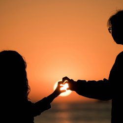 Silhouette of child and parent making heart shape with their hands as the sun is setting