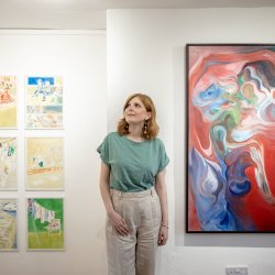 Workshop leader Alicja stand in front of some of her artwork .  The larger print is brightly coloured