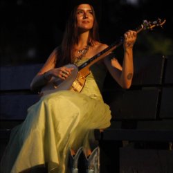Johanna Wacker seated in a Yellow Dress Holding a Banjo while looking toward the sky.