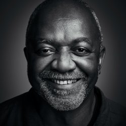 A black and white photo of a smiling man with a short grey beard