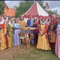 Coro Monti Azzurri performers in colourful Renaissance costumes pose together beside a medieval-style tent before their concert.
