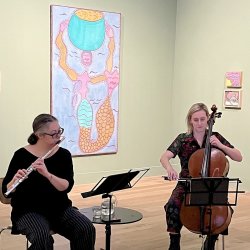 Two people performing in a gallery space, one playing the flute and the other the cello