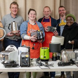 A group of people holding electrical appliances that have been fixed at the Fixing Factory