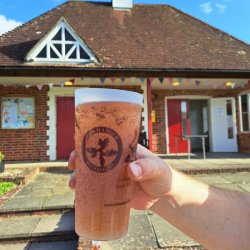A hand holding a pint of beer in front of a village hall