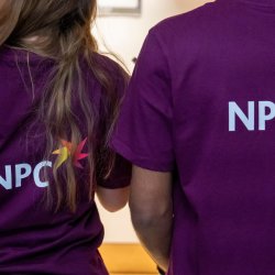 two NPC employees wearing purple t shirts that have the NPC logo on the back