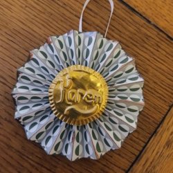A paper concertina decoration with carved metal coin on the front reading Karen