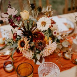 Autumnal flowers sit in the centre of a wedding table surrounded by candles and glassware