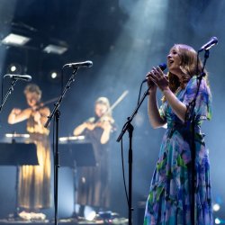 Beth singing on stage with two fiddlers in the background