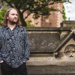 Dr James Wright stands in front of historic stone masonry