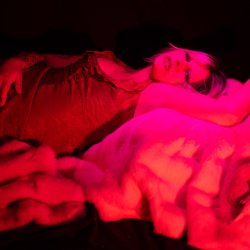 A blonde woman in a red dress reclines on a fur rug