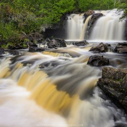 A photo of a waterfall and small stream surrounded by green trees.