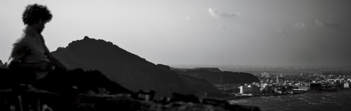 Man (L) sitting on mountain looking down (R) to the coastal Yemeni city of Aden. Credit: Sayed Asif Mahmud