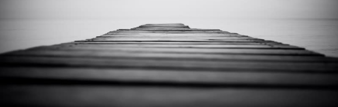 a long-shot close up of jetty planks heading out to the water in greyscale