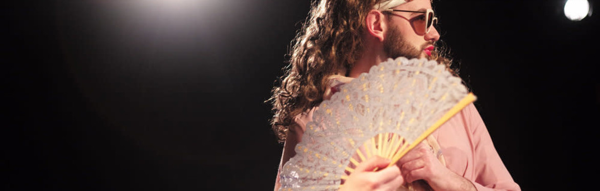 A bearded drag queen with a fan