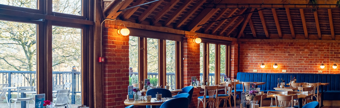 Image of a warm lit restaurant interior with blue chairs and a large window facing Leeds Castle.