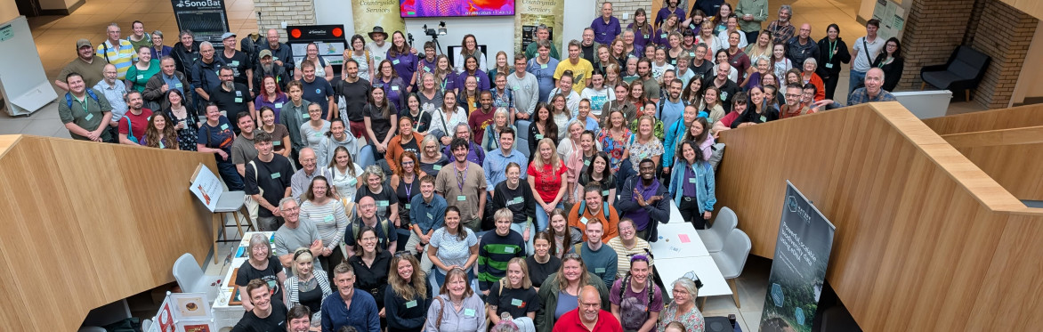 Crowd of delegates at the National Bat Conference 2025 smiling up at the camera among the exhibitor stands