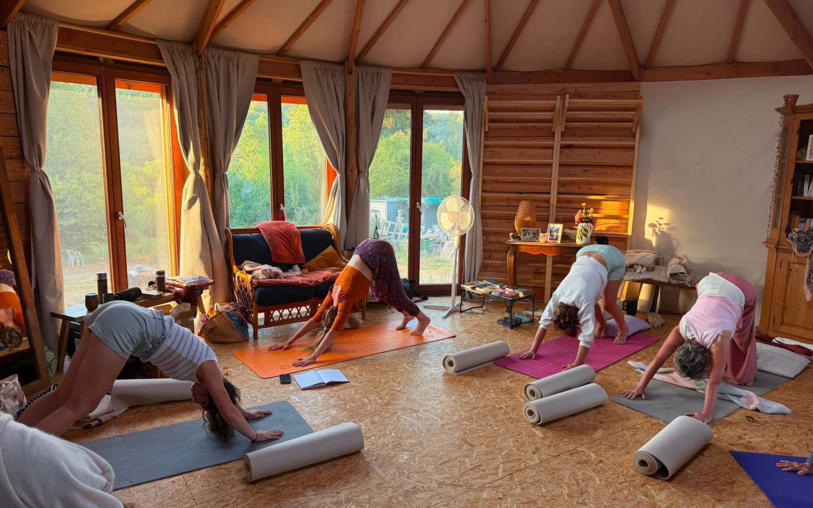 Group of people practicing a standing side-bend yoga pose on mats in a bright wooden yurt at Radhadesh