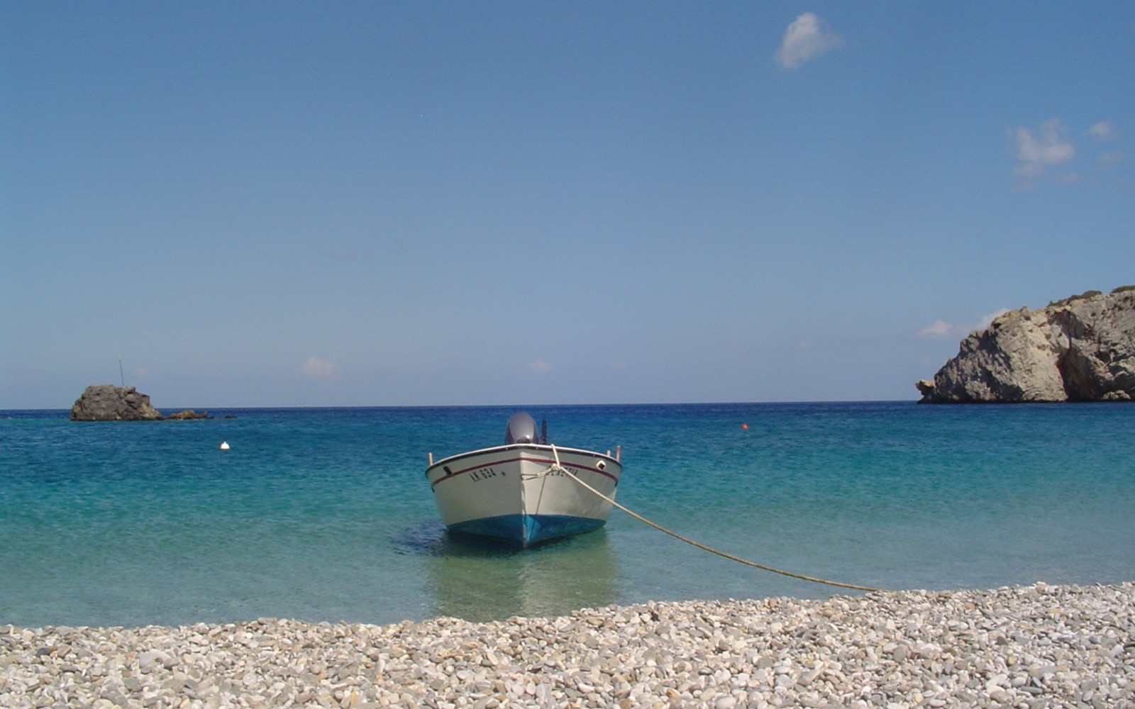 a fishing boat on the sea next to a pebble beach