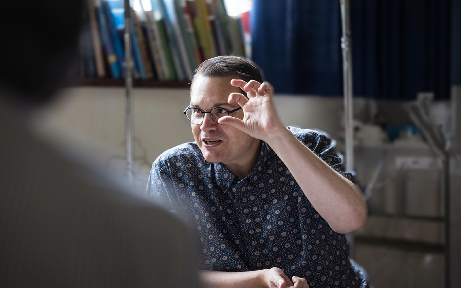 Composer Paul Mealor gestures expressively as he leads a masterclass, speaking with a participant seated in the foreground.