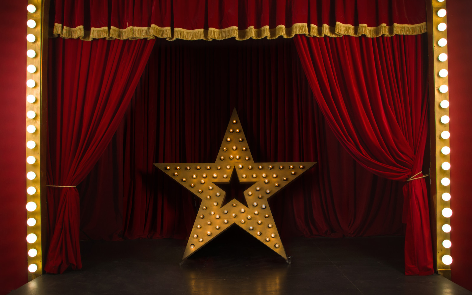 Theatre stage with red curtains and a large star sculpture covered in light bulbs