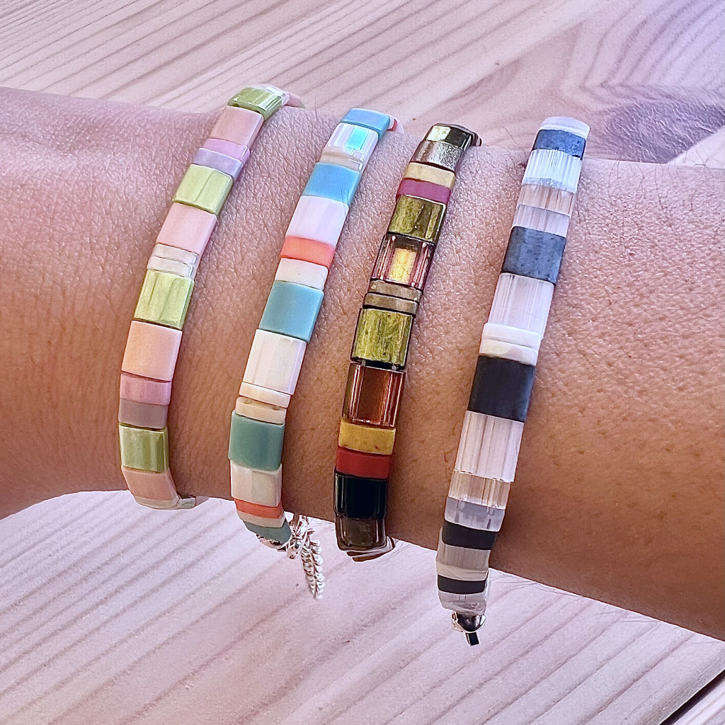 A stack of 4 colourful beaded bracelets. The beads are square-shaped and are in various colours of blue, green, orange, pink and purple.