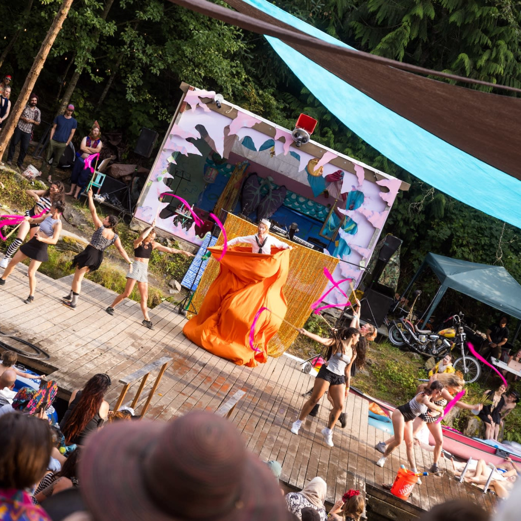 An outdoor scene of a crowd of cheering people on the left and a soapbox derby car with two costumed riders on the right