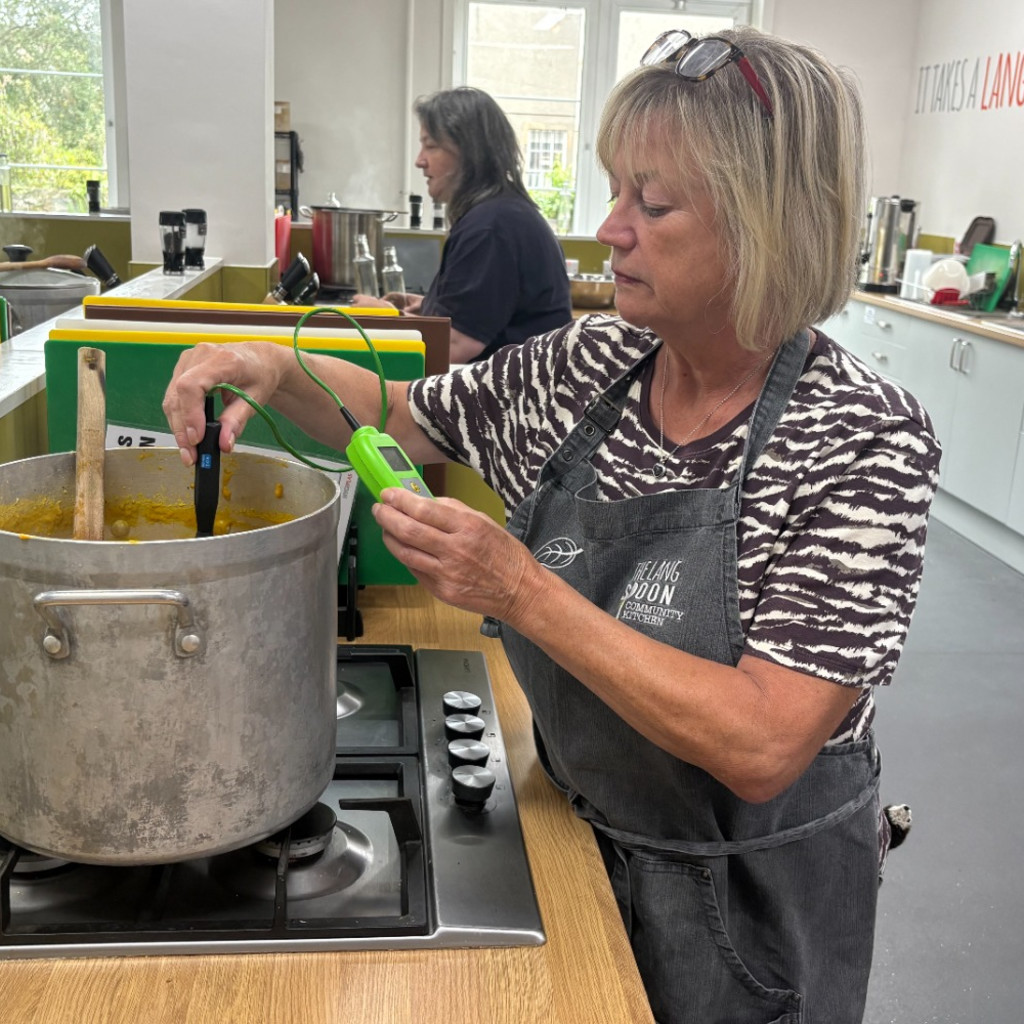 A woman's hand slicing yellow and red peppers on a green chopping board.