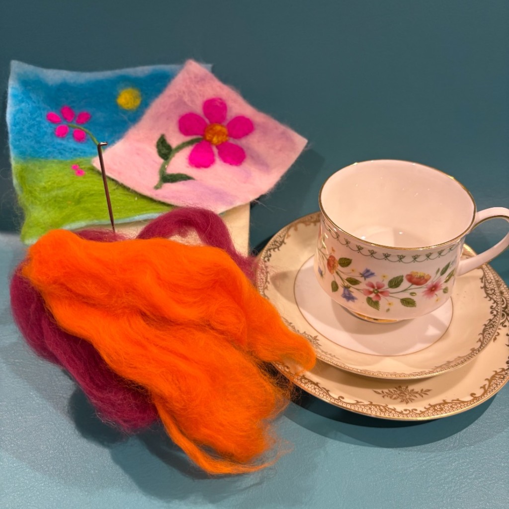 Needle felting yarn, sponge and needle next to a vintage tea cup and saucer