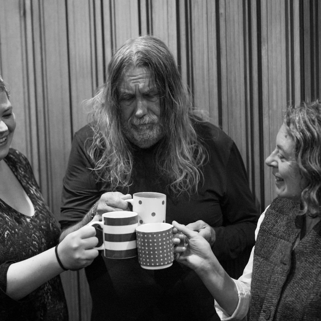 Black and white image of Hannah Cumming, Paul Hutchinson and Karen Wimhurst clinking mugs