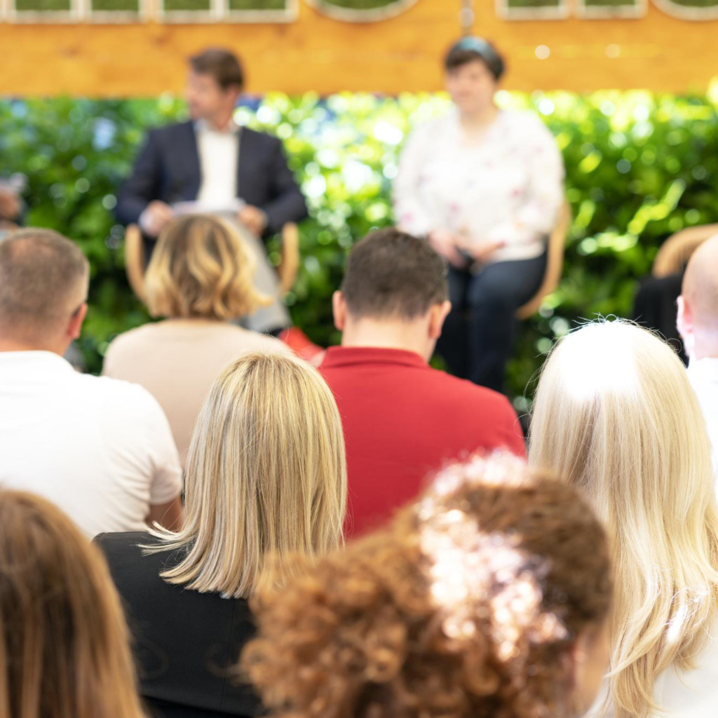 En publik med personer där man ser ryggarna och som sitter och lyssnar på personer i en panel.