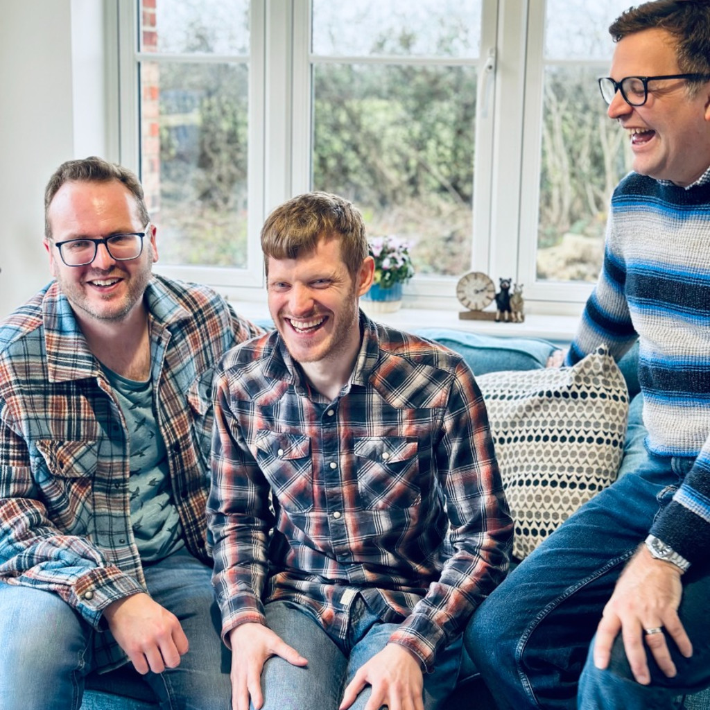 The Young'uns sitting on a green sofa wearing colourful checked shirts and laughing.
