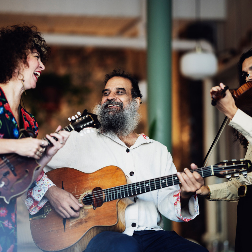 The image features Duane Andrews and two members of the Hot Club of Conception Bay performing with their instruments and smiling at each other.