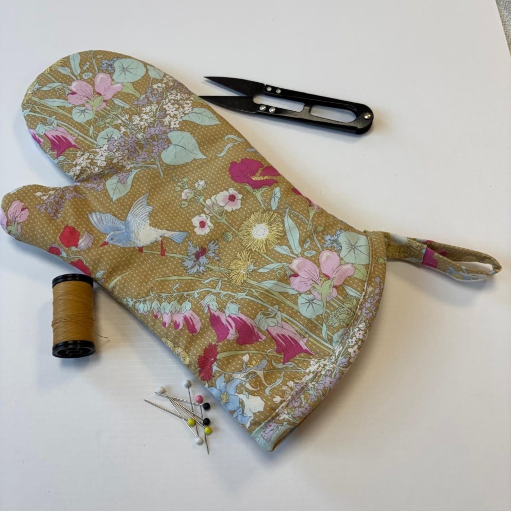 A completed oven mitt with a pair of snips, some pins and a roll of thread