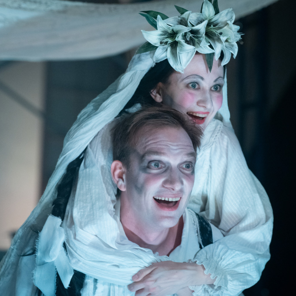 Yana Gladkikh as Leah, with flowers on her head, riding on the back of Andrey Burkovskiy as Khonen, both smiling