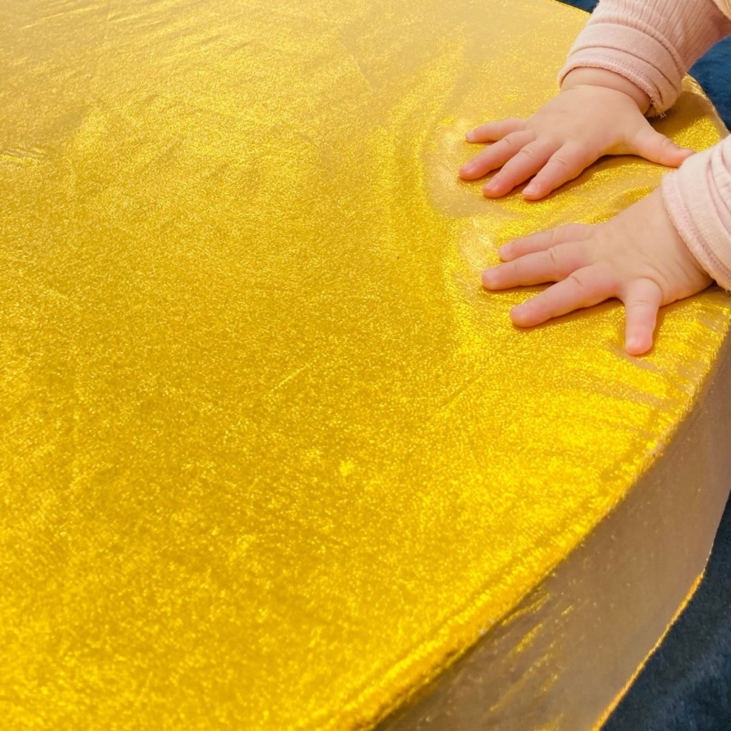 A baby's hands touching a golden piece of material