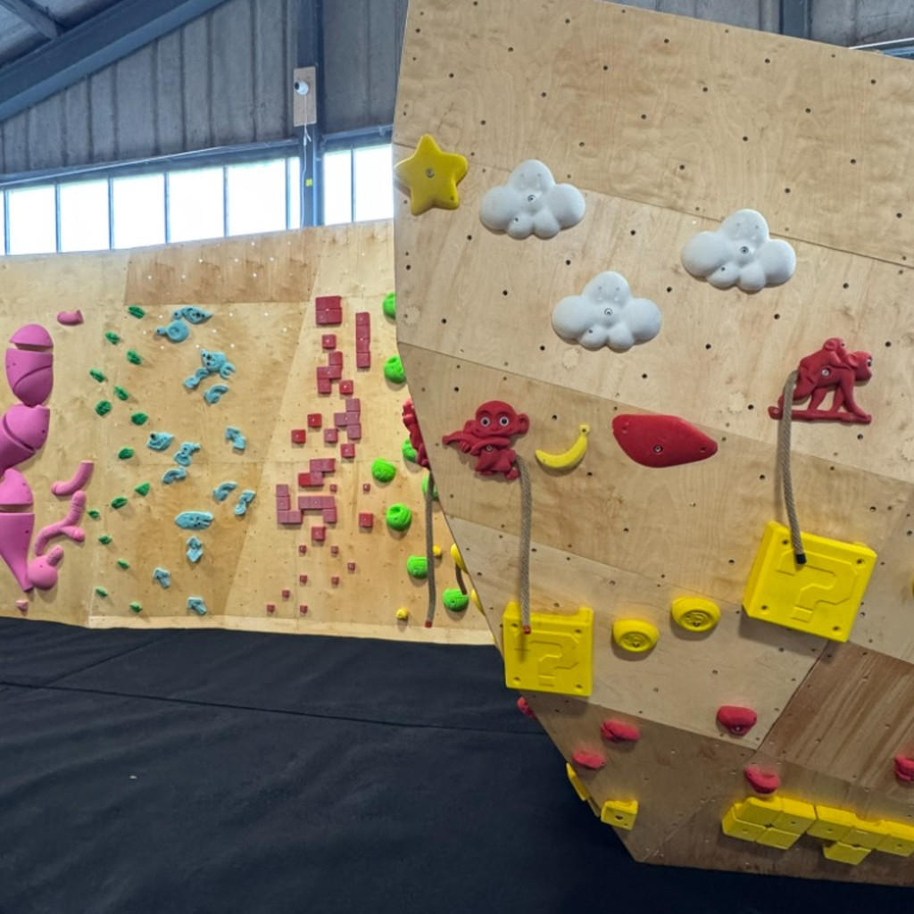 Image of the bow of a boat shaped climbing structure, set with monkey, cloud and super mario themed climbing holds, and more climbing in the background.