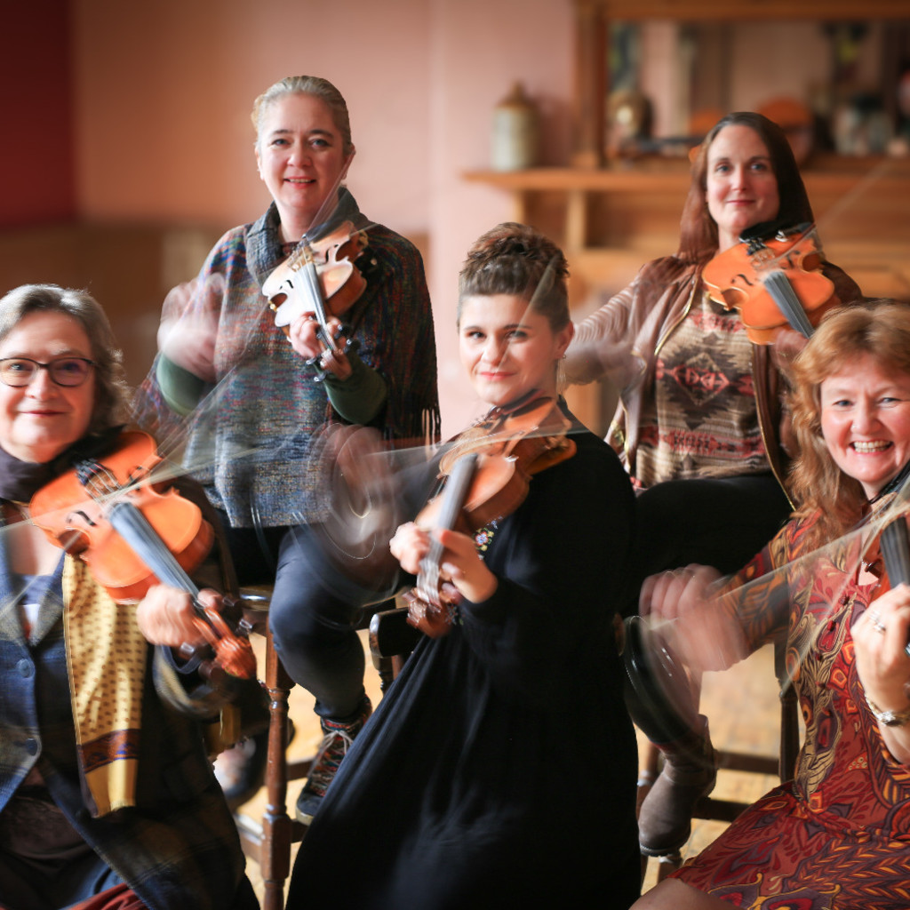 The image features Fi Fraser, Jess Arrowsmith, Nancy Kerr, Rosie Butler-Hall, and Sarah Matthews sitting on stools in two rows playing fiddle and smiling at the camerao