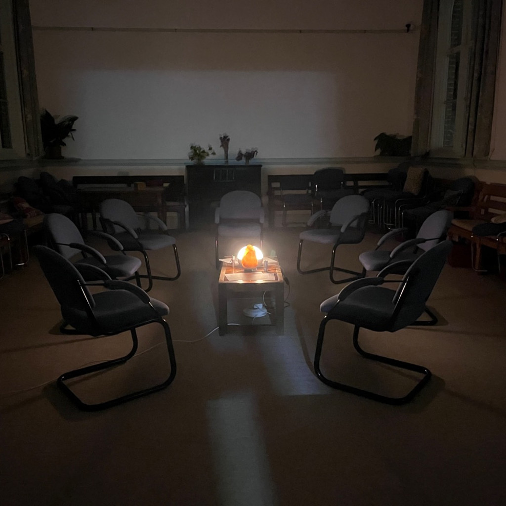 A dimly lit room with a circle of chairs around a warm, glowing light