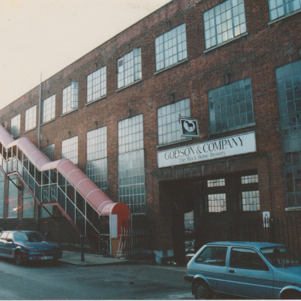 an image of the front facade of Chisenhale Dance Space in 1980, a brick warehouse with square glass windows and a red fire escape.
