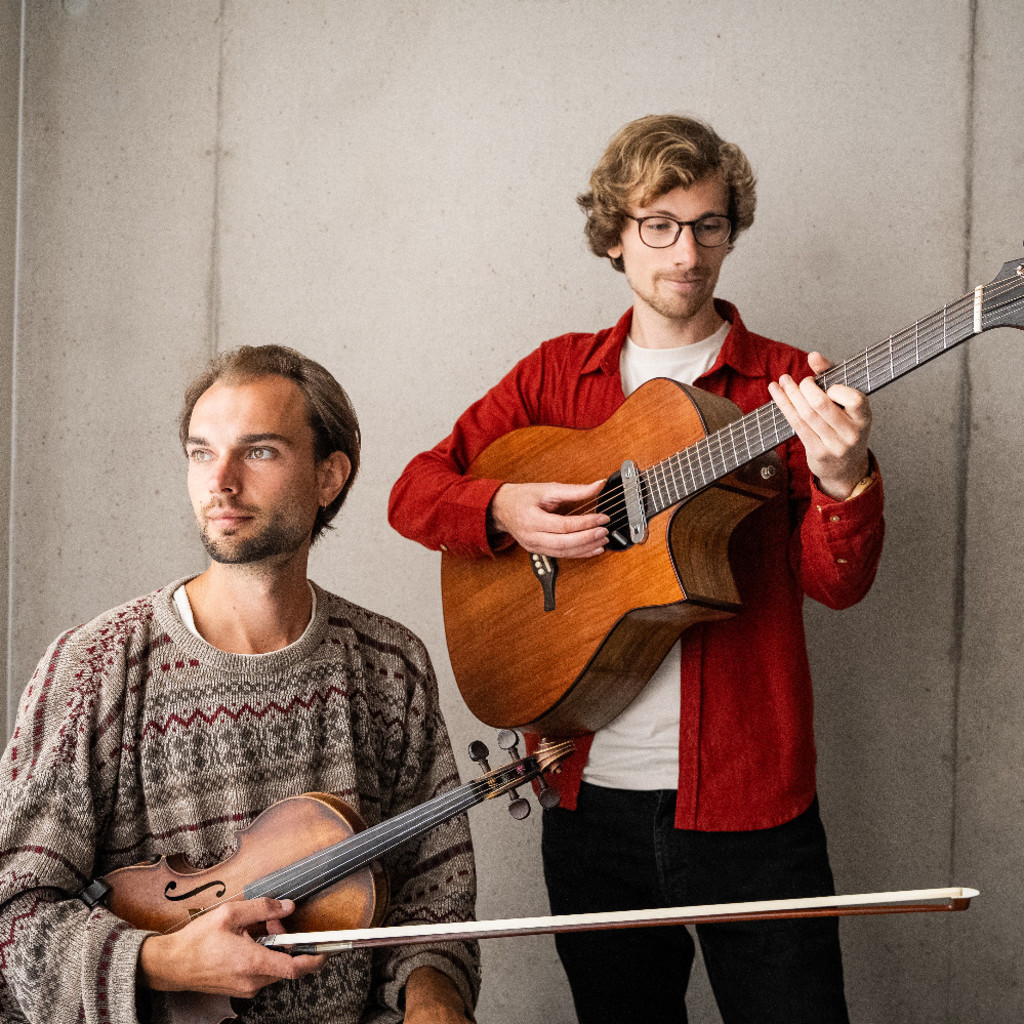 The image features Seth Bye holding a fiddle looking off to the left, sitting on the left of Chris Avery, who is standing holding a guitar looking at the fret board. Both are in front of a white wall.